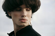 © Daria Chacheva/Stocksy - Handsome man with an earring in black clothes on the sky background.