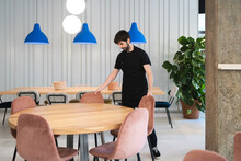 Young Man Tidying Chairs In Cafe Before Opening
