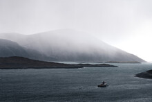 A Fishing Boat At Sea With Rain Coming Over Mountains