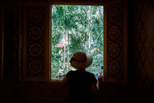 Woman In Sunhat Looking Out From Temple Window In Xishuangbanna, China