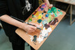 © Ezequiel Giménez/Stocksy - Crop artist with paint palette and paintbrush in studio