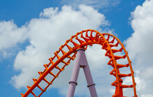 Curved Of Orange Roller Coaster Track In Close Up Isolated On Cloudy Blue Sky Background.