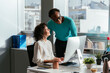 © David Prado/Stocksy - Focused woman working on computer in office discussing with colleague