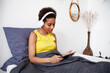© Elena Kharichkina/Stocksy - A young girl relaxes with a tablet and headphones on the bed