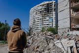 Fototapeta  - Chernihiv Ukraine 2022: a guy looks at the ruins after an air strike. Rear view. The building was destroyed after the air strike. Ruins during Russia's war against Ukraine.