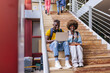© VICTOR TORRES/Stocksy - Cheerful multiethnic students using laptop on stairs