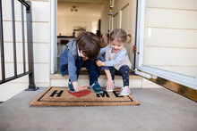 Children Laughing And Sitting On Front Porch Of Home With Welcome Mat