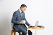 Indian business man wear suit using laptop while holding coffee mug in hand, Asian corporate guy working on computer sitting on chair looking at camera isolated on white studio background