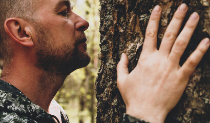 Wall Mural - Adult man touches a huge tree, sniffs the bark and hugs the trunk. An adult man enjoys being alone with nature in the forest. The concept of nature conservation, forests, ecology. Human and nature.