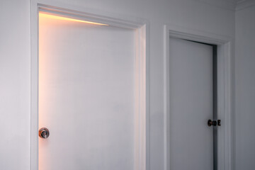 minimalist architecture or metaphor of choosing between two alternative options, interior corridor with two white doors left ajar and light shining from inside one of them