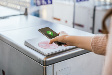 Woman's hand ticking her transport ticket in the machine with her mobile phone on train station. NFC and contactless technology concept