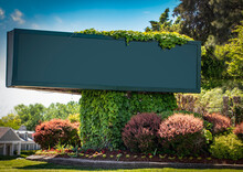 Large Advertising Sign -blank And Copy Space - On Corner Landscaped With Vines And Flowerbeds With Trees And Buildings In Background