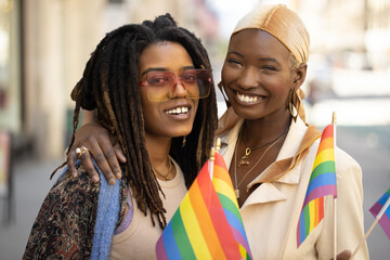 Sticker - LGBTQ same sex black women lesbian couple waving rainbow flags on a city street