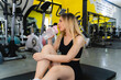 A young woman is stretching and drinking water in the gym after a workout during the day