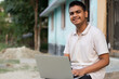 Portrait of young teenager rural area student using laptop smelling looking on camera.