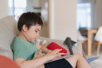 Wall Mural - Young boy using tablet playing game on internet, Kid sitting on sofa watching or talking with friend online,Child relaxing in living room in the morning, Children with New Technology concept