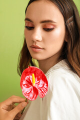 Wall Mural - Beautiful young woman looking at anthurium flower in her hand on green background