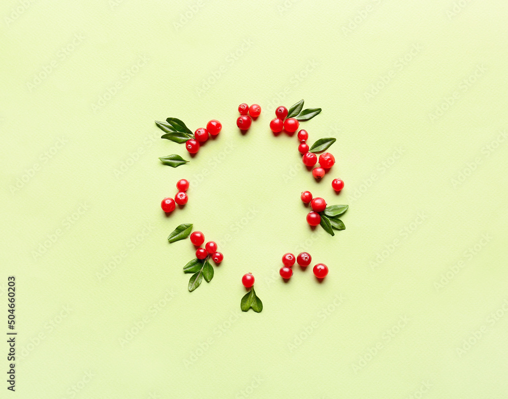 Frame made of red lingonberries with leaves on green background