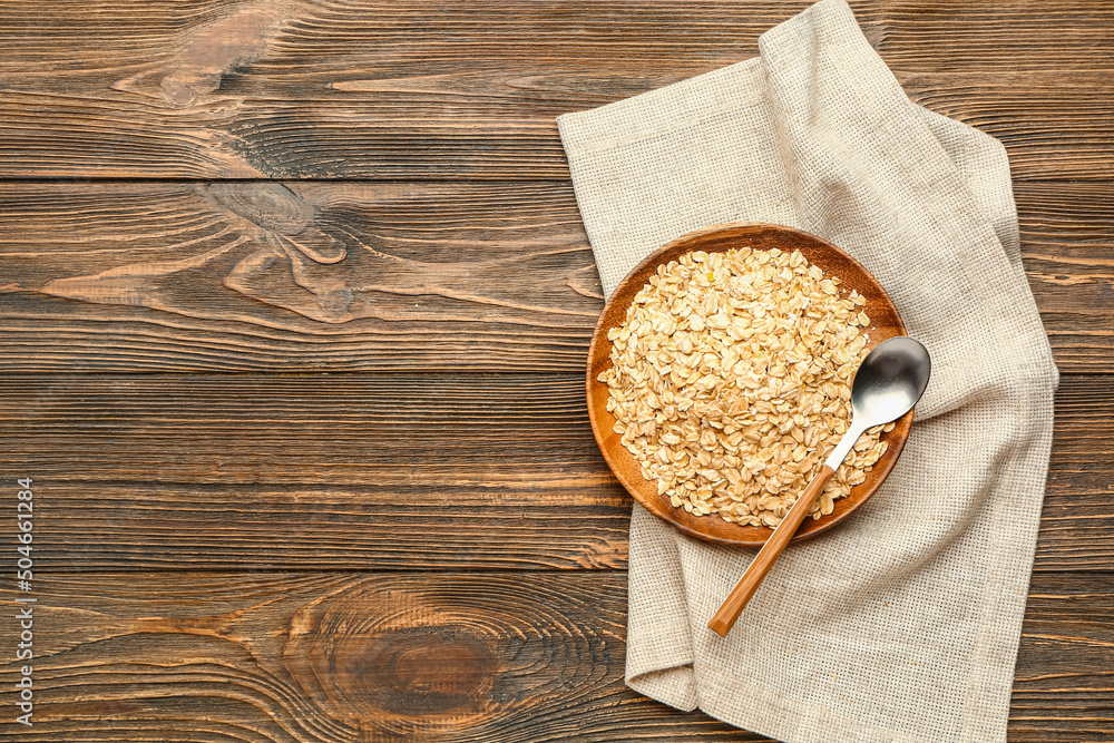 Plate of raw oatmeal and spoon on wooden background
