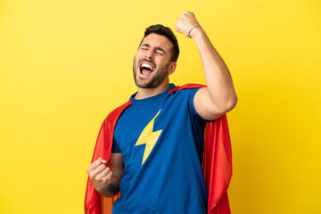 Young handsome caucasian man isolated on yellow background in superhero costume and celebrating a victory