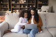 © fizkes - Family do e-shopping at home, caring parent teach kid use device, spend leisure enjoy educational content on internet concept. African woman and little preschool daughter using laptop seated on couch