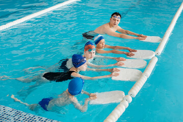 Wall Mural - A group of boys and girls train and learn to swim in a modern swimming pool with an instructor. Development of children's sports. Healthy parenting and promotion of children's sports.