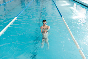 Wall Mural - A coach teaches a seven-year-old boy to swim in a modern swimming pool. Learn to swim. Development of children's sports. Healthy parenting and promotion of children's sports.