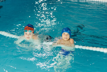 Wall Mural - A group of boys play and learn to swim in a modern swimming pool. Development of children's sports. Healthy parenting and promotion of children's sports.