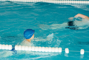 Wall Mural - A group of boys play and learn to swim in a modern swimming pool. Development of children's sports. Healthy parenting and promotion of children's sports.