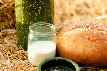 Glass jar with milk and broken bread on a background of straw on the Ukrainian field. Harvest.