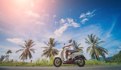 Wall Mural - Stylish young man rides a motorbike on the road near the sea and palm trees