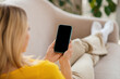 © Prostock-studio - Young european woman looking at phone with blank screen, searching info, sitting on sofa in living room