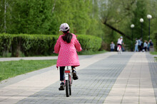 Kid Girl Riding On A Bicycle On A Path In A Green Park. Child Cyclist, Spring Or Summer Leisure