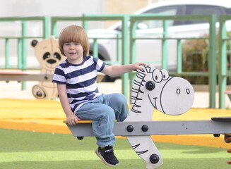 Happy baby child riding a toy white horse at the playground. Boy 3 years with long hair