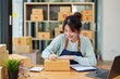 © Jirapong - A portrait of a small startup, and SME owner, an Asian female entrepreneur, is writing down information on a notepad to organize the product before packing it into the inner box for the customer