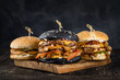 A set of craft juicy burgers on wooden cutting board on a smoky black background. trung on wooden skewers. Tasty grilled cheeseburgers with beef cutlet, tomato, cheese and lettuce. 