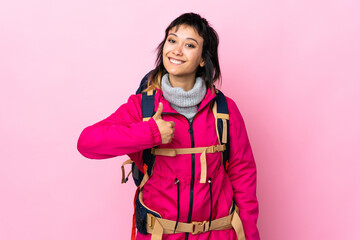 Wall Mural - Young mountaineer girl with a big backpack over isolated pink background giving a thumbs up gesture