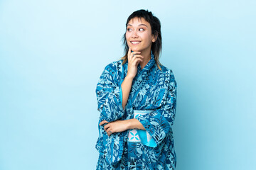 Wall Mural - Young woman wearing kimono over isolated blue background thinking an idea while looking up