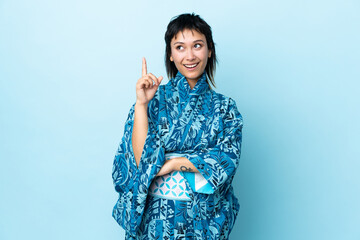 Wall Mural - Young woman wearing kimono over isolated blue background pointing up a great idea