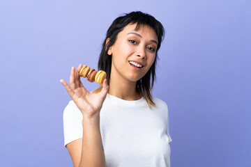 Wall Mural - Young Uruguayan woman over isolated purple background holding colorful French macarons and smiling a lot