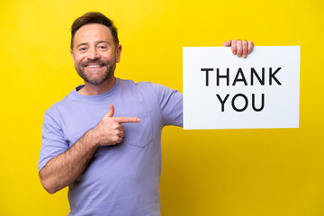 Middle age caucasian man isolated on yellow background holding a placard with text THANK YOU and  pointing it