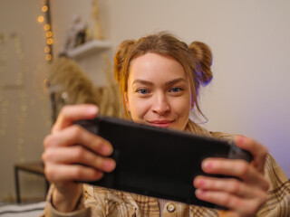 Wall Mural - Close-up. A fair-haired girl gamer plays a fun video game online with friends. New modern technologies, entertainment on the road, travel, virtual reality, cyberspace.