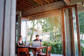 Wall Mural - Coworking and freelance concept. Young  bearded man  and young woman working together on laptop computers while sitting on cafe terrace.