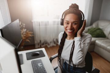 Wall Mural - close up of happy young mixed-race smiled female in headphones sitting at desk in living room