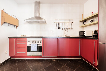 Apartment kitchen with red cabinets with drawers and doors, stainless steel handles, black wood countertops and black slate flooring