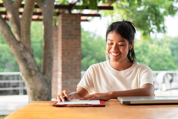 Latin woman reviewing documents smiling. College student doing homework on campus. Copy space.