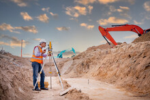 Surveyor Engineer Wearing Safety Uniform ,helmet And Radio Communication With Equipment Theodolite To Measurement Positioning On The Construction Site Of The Road With Construct Machinery Background