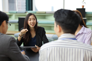 Collaborative process of young asian business people team working together discussing, researching, brainstorming and planning work at business meeting in modern office building and city background