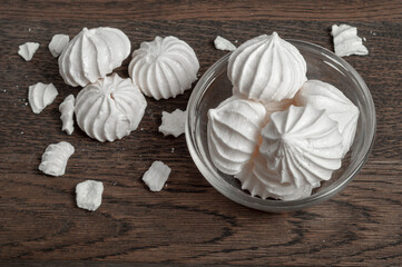 dessert from the French bezier lies in a glass vase on a dark wooden board. there are whole and broken meringues lying around, flatlay.