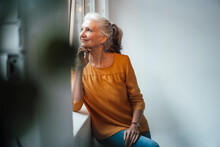 Smiling Senior Woman With Hand On Chin Standing By Window